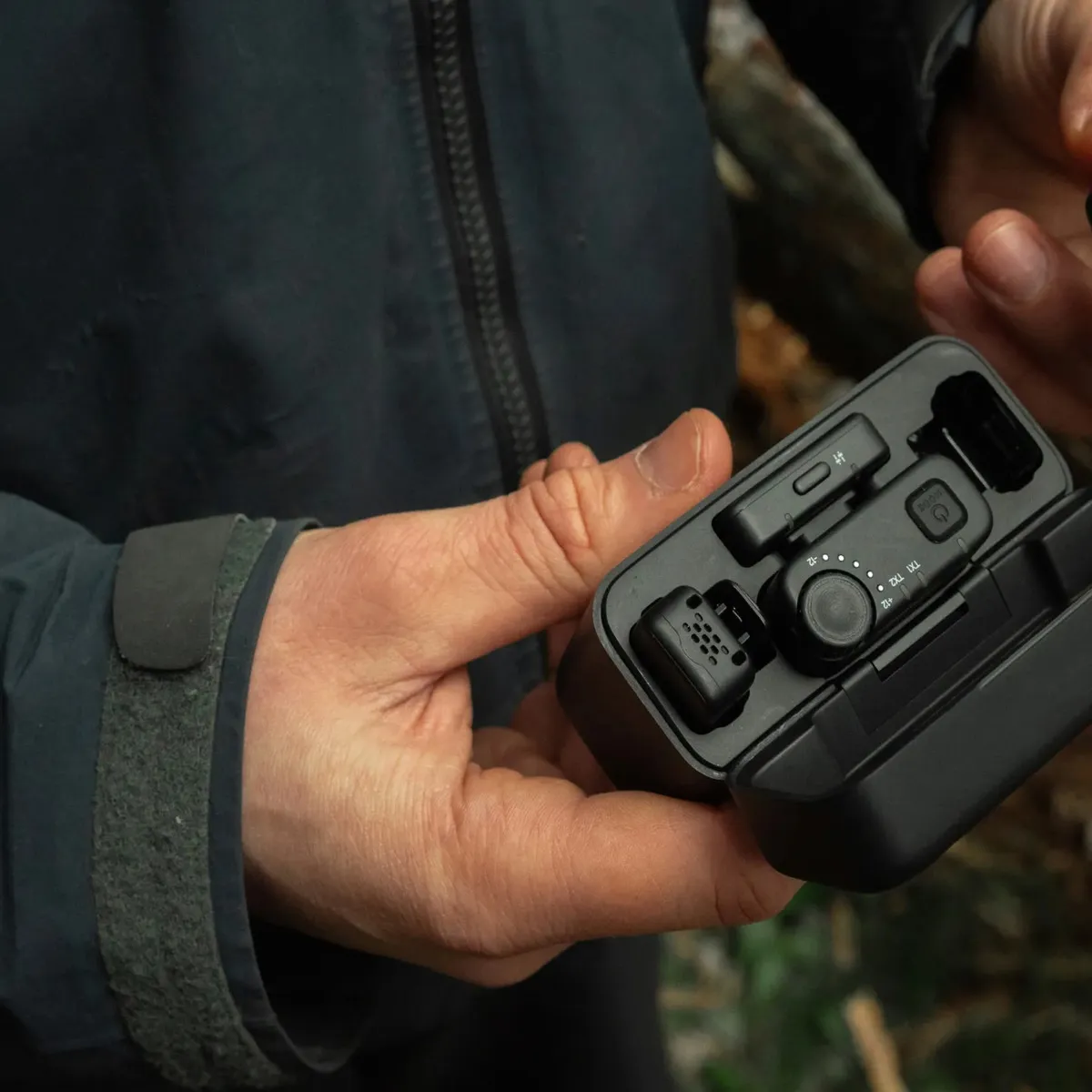 Hands lifting a GoPro wireless mic transmitter from the open charging case outdoors.