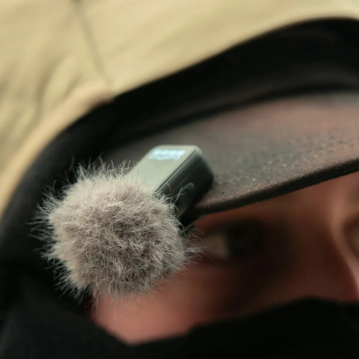 GoPro wireless mic transmitter with windscreen fitted, clipped to the brim of a cap for close-up voice capture.