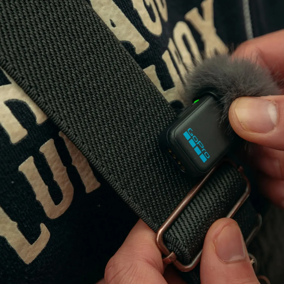 GoPro wireless mic transmitter with windscreen being clipped to a bag strap.