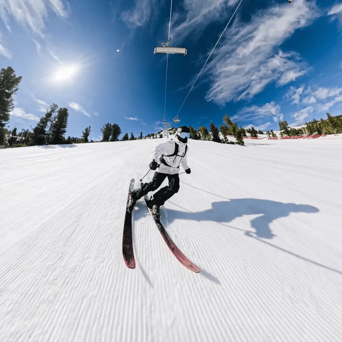 Skier carving down a groomed run filmed from an extension pole on a ski pole.
