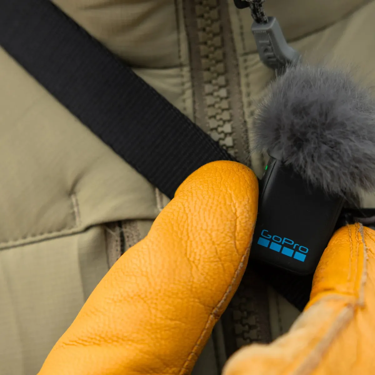 Gloved hands attaching the GoPro wireless mic transmitter to a jacket zip in cold weather.